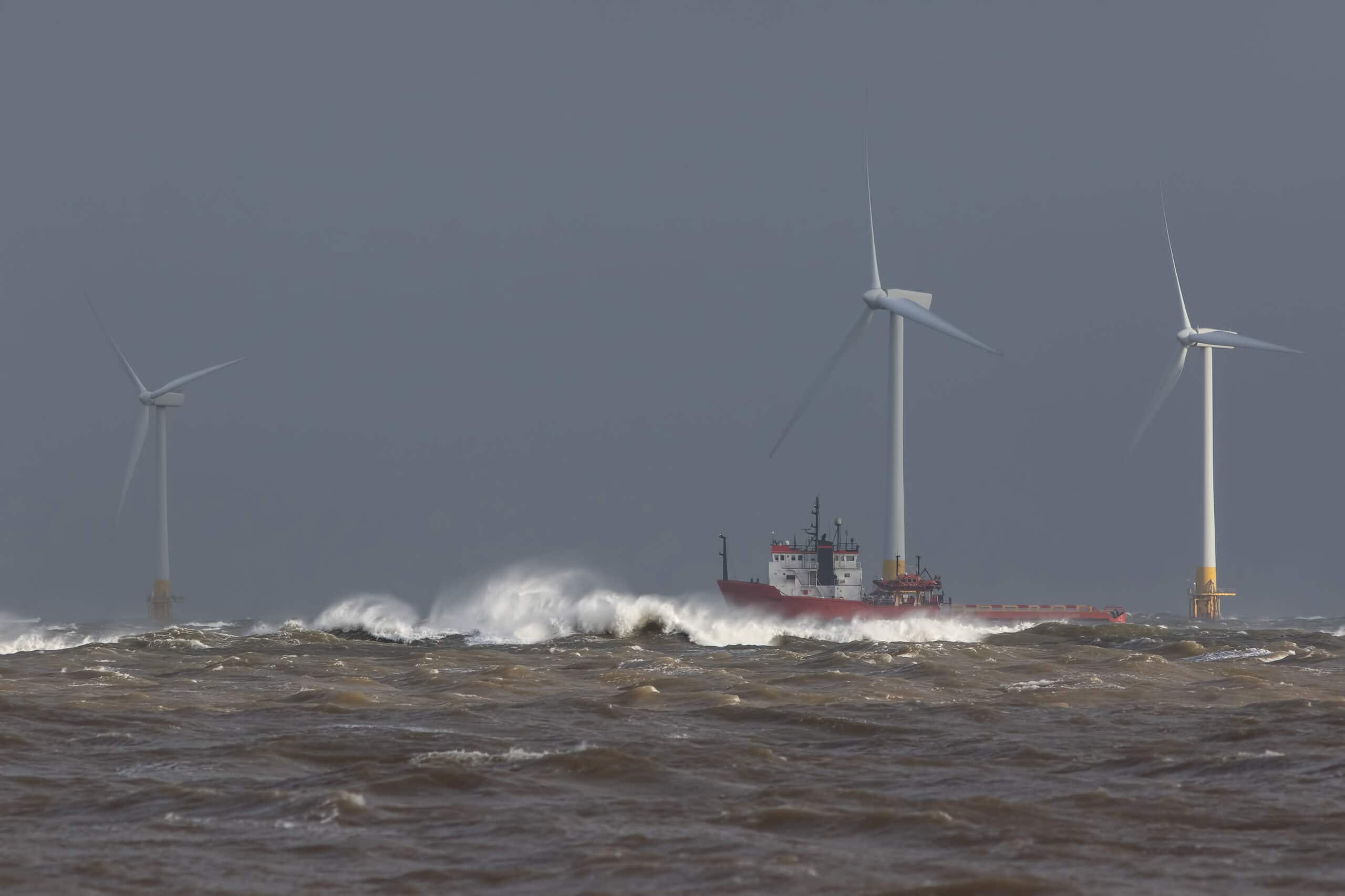 Ship sailing in rough sea around offshore wind farm turbines.