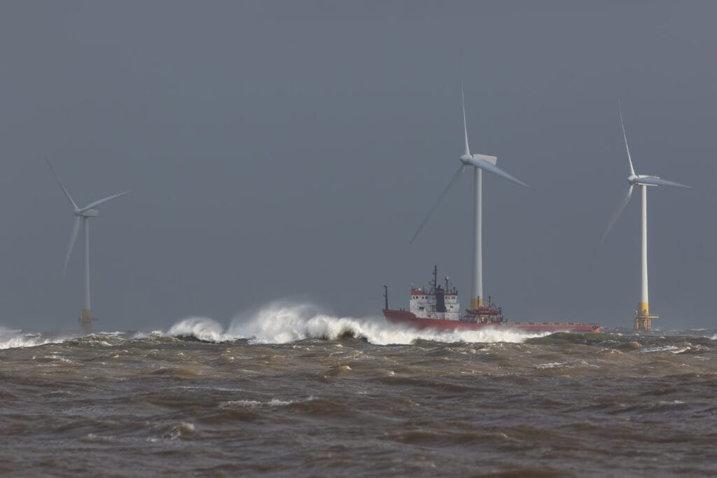 Ship sailing in rough sea around offshore wind farm turbines.