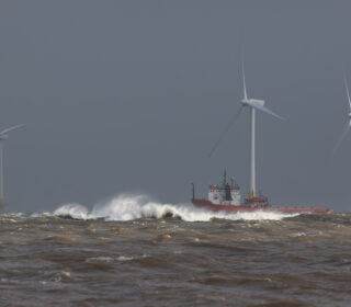 Ship sailing in rough sea around offshore wind farm turbines.