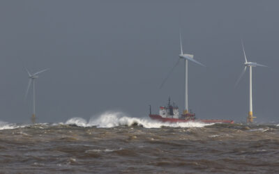 Ship sailing in rough sea around offshore wind farm turbines.